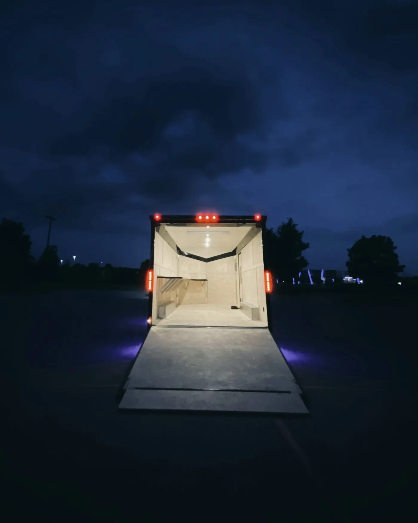 Offener, beleuchteter Anhänger mit heruntergelassener Rampe auf einem Parkplatz bei Nacht
